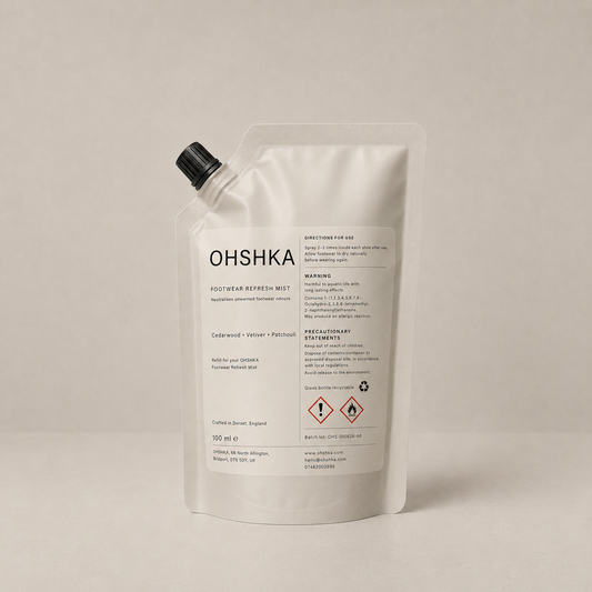 A white refill pouch of OHSHKA Footwear Refresh Mist with a black spout cap, photographed on a neutral light beige background.